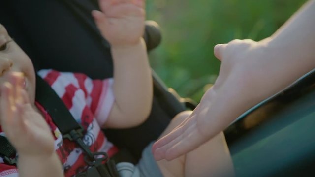 Mom playing with her baby boy sitting in stroller, giving son high five and smiling slow motion 4k