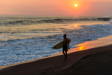 Silhouette of surfer walking on beach at sunset