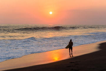 Naklejka premium Sylwetka surfer spaceru na plaży o zachodzie słońca