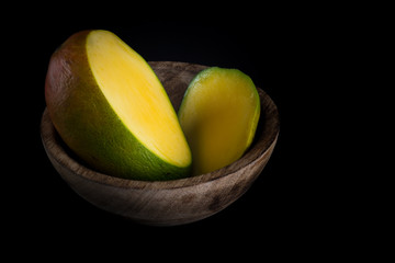 Sliced mango in a natural handmade wood bowl isolated on black background