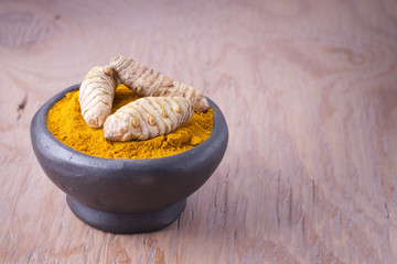 Roots and turmeric powder on wood background (long curcuma)