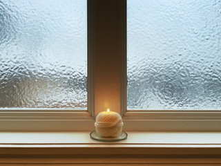 Fototapeta na wymiar Candle on windowsill of a frosted window
