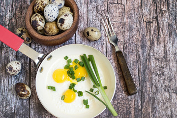  A small frying pan with scrambled eggs, a wooden bowl with quail eggs and a fork on an old table.