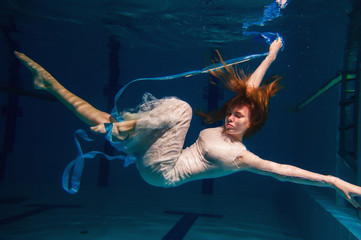 young girl in beautiful white dress posing underwater in the pool 