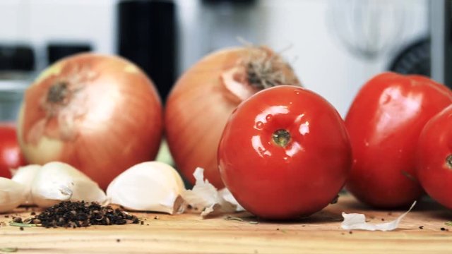 Close-up tomatoes, onions, garlic, and herbs in a kitchen, pan left