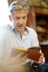 Mature man reading book in armchair at home