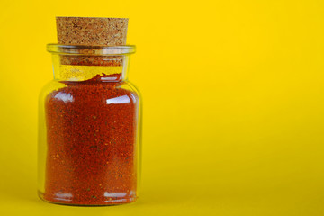 mixture of red chili peppers and paprika in a glass bottle on a yellow background