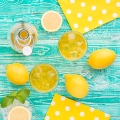 lemonade or limoncello in glasses with ice cubes, sherbet glass with ice cubes, bottle with drink, lemon fruits on turquoise colored wooden table, top view - 148704030