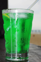 Close up of fresh summer drink, mint with carbonated water, ice cubes and lemon slices against the background of a quiet sea. Concept Summer.