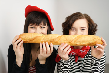 zwei lachende frau halten ein baguette vor ihr gesicht