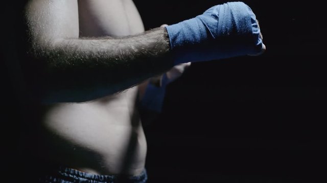 Tilt up of shirtless muscular sportsmen standing isolated on black background and putting wrist straps on before practice 