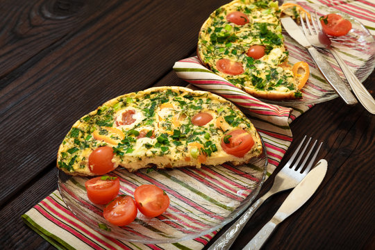 Omelette with greens, tomatoes and sweet pepper for breakfast in a glass plate on a dark wooden table