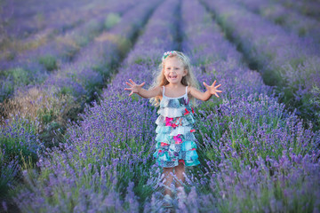 Young mother with young daughter smiling on the field of lavender .Daughter sitting on mother hands.Girl in colorful dress and mother in dark blue dress.