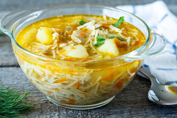 Home chicken soup with noodles and vegetables in a glass bowl.
