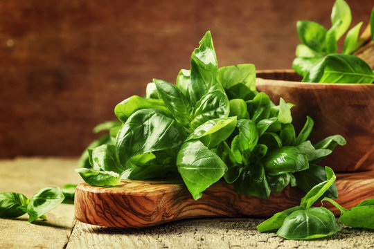 Fresh green basil in olive mortar with pestle, vintage wooden background, rustic style, selective focus