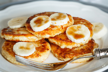 Homemade cottage cheese pancakes with caramel (honey) and banana on a white plate.