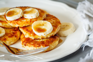 Homemade cottage cheese pancakes with caramel (honey) and banana on a white plate.