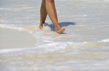 Vacation concept image. A tanned caucasian woman is walking barefoot on the beaches of the Caribbean sea. Foamy waves with white sand.