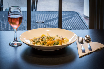 Shrimp and Linguine Entree and Wine: Plated shrimp fettuccine entree with Parmesan cheese and a Rose wine under warm soft light.