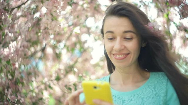 Happy woman with a phone in a blooming spring garden