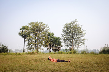 Indian man sleeping on the grass in the middle of the day.