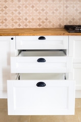 Opened kitchen drawer, kitchen in a traditional style with wooden white facade, black handles and wooden countertop 