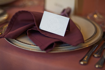 White empty card stands on dark red napkin on dinner plate