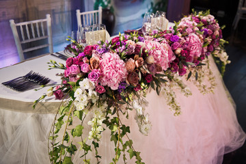 Garland of roses and hydrangeas hangs from dinner table covered with beige cloth