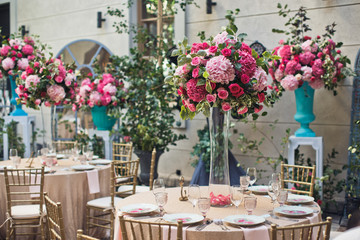 Round beige tables decorated with pink flowers stand on the backyard