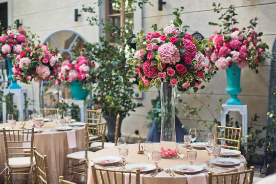 Round beige tables decorated with pink flowers stand on the backyard