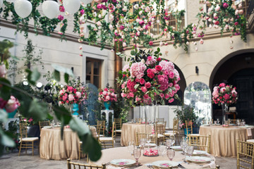 Round dinner tables with pink flowers stand on beautiful decorated backyard