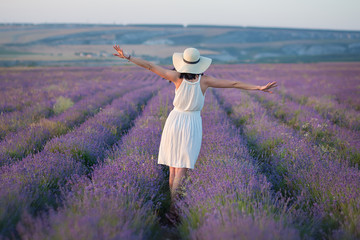 Young beautiful lady with lovely face walking on the lavender field on a weekend day in wonderful dresses and hats.