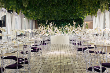 Round tables and violet chairs stand under the ceiling of greenery