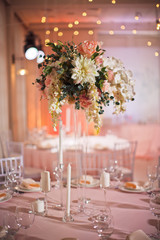 Tall vase with beautiful bouquet stands in the middle of dinner table