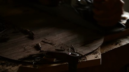 Luthier sandind a back of a new guitar with a wood planer in the workplace