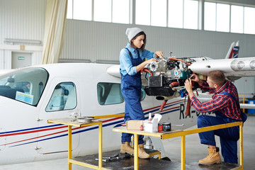 Airplane service crew repairing plane in hangar:  two young mechanics, man and woman, fixing jet...
