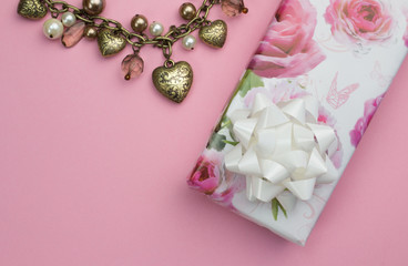Obraz na płótnie Canvas Background with gold heart and pearl necklace, wrapped rose gift wrapped present isolated on pink background - love background