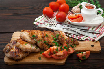 Sliced grilled pork barbecue meat on wooden cutting board over dark background