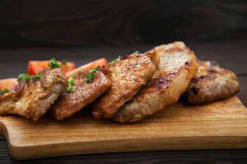 Sliced grilled pork barbecue meat on wooden cutting board over dark background