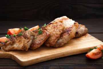 Sliced grilled pork barbecue meat on wooden cutting board over dark background