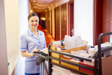 Young female with tidy supplies standing in hotel corridor