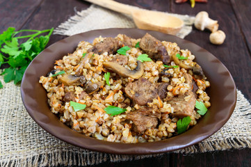 Buckwheat porridge with pieces of meat  and mushrooms on a dark wooden background.