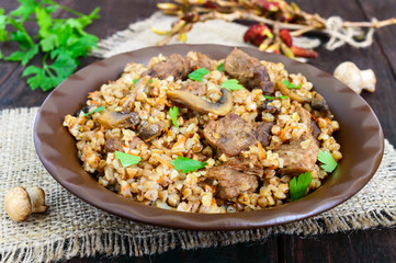 Buckwheat porridge with pieces of meat  and mushrooms on a dark wooden background.