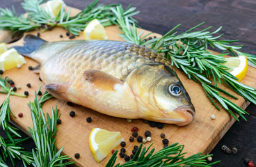 Big live carp (crucian) on a cutting board with rosemary branches. Fresh catch. Close up