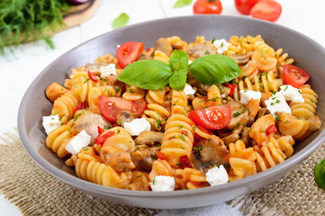 Pasta Radiatori with chicken, mushrooms, cherry tomatoes, feta cheese and tomato sauce on a white wooden background.