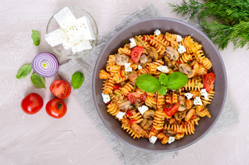 Pasta Radiatori with chicken, mushrooms, cherry tomatoes, feta cheese and tomato sauce on a light background. Top view.