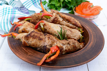 Meat rolls stuffed with sweet pepper, carrots in a clay bowl on a white wooden background.