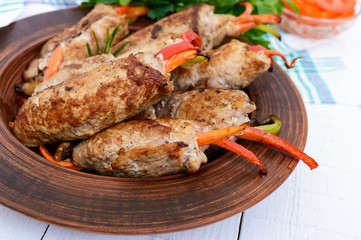 Meat rolls stuffed with sweet pepper, carrots in a clay bowl on a white wooden background. Close up
