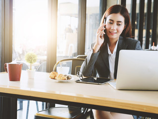 Charming businesswoman talking with smartphone and look at laptop while working at cafe