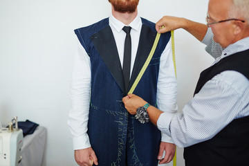 Old fashioned tailor measuring model in small atelier studio to make custom classic suit with jacket